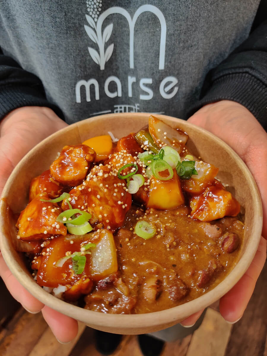A close up image of someone with Marse apron and holding a bowl of Marse rice combo